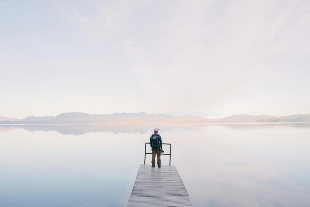 A solitary traveler stands on a dock enjoying the serene water view